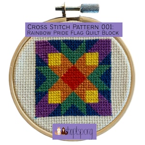May include: A cross stitch pattern for a rainbow pride flag quilt block. The pattern is stitched on white Aida cloth and framed in a wooden embroidery hoop. The colors of the rainbow are represented in the pattern, with a red center and yellow, orange, green, blue, and purple surrounding it.