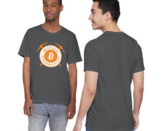 May include: Dark gray t-shirt featuring a Bitcoin logo in an orange circle with the text "Bitcoin in Blockchain we trust" and two crossed pickaxes. The shirt is a crew neck and short-sleeved.