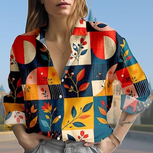 May include: A colourful button-down shirt with a geometric design. The pattern includes squares and semi-circles in red, yellow, blue, and cream, with floral and leaf elements. The long-sleeved shirt has a V-neck and is made of a lightweight material.