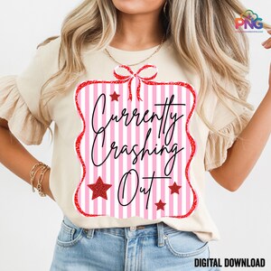 May include: A beige t-shirt with a pink and white striped graphic that reads "Currently Crashing Out" in black script. The graphic is framed with a red glitter border and includes red glitter stars. The words "Digital Download" are at the bottom.