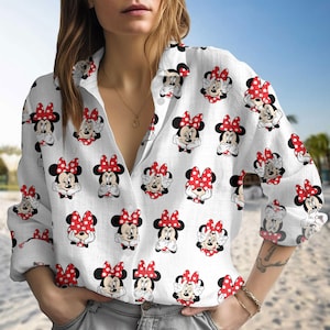May include: White button-down shirt with a repeating pattern of Minnie Mouse illustrations. Each Minnie Mouse has a red polka-dot bow. The shirt has long sleeves and a collared neckline.