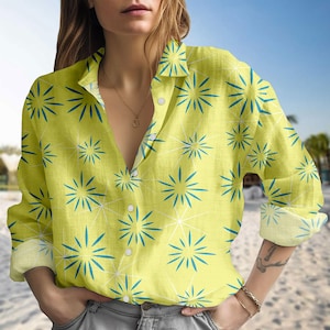Puede incluir: Camisa abotonada de color amarillo claro con un estampado de estrellas azules y líneas blancas. La camisa de manga larga tiene cuello y está hecha de una tela ligera.