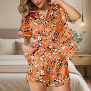 May include: Orange pajama set featuring a pattern of Disney characters in Halloween costumes. The short-sleeved top and shorts have white trim. The set includes Mickey Mouse, Donald Duck, and Goofy.
