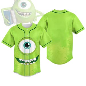 Könnte beinhalten: Ein hellgrünes Baseball-Trikot mit einem großen Cartoon-Auge und einem lächelnden Mund. Das Trikot hat eine Knopfleiste vorne und dunkelgrüne Paspeln. Die Rückseite des Trikots ist einfarbig hellgrün. Das Design ist von einer beliebten Zeichentrickfigur inspiriert.