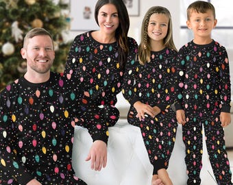 May include: Matching black Christmas pajamas with colorful string light and snowflake patterns. The family is wearing long-sleeved tops and pants. The pajamas are a festive and comfortable choice for the holiday season.
