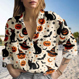 May include: A Halloween-themed button-down shirt. The cream-coloured shirt is patterned with orange pumpkins, black cats, witch hats, bats, stars, and crescent moons. The long-sleeved shirt has a collared neckline and button closure.