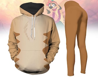 Pode incluir: Um moletom bege com capuz preto e bolso canguru, combinado com leggings marrons. O moletom com capuz apresenta um design que se assemelha a um personagem de desenho animado. As leggings são de cor marrom lisa. O fundo é um gradiente suave de rosa e laranja.