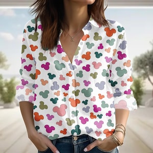 May include: White button-down shirt with a colorful Mickey Mouse pattern. The long-sleeved shirt features a V-neck and is adorned with various shades of orange, pink, green, and purple Mickey Mouse silhouettes.