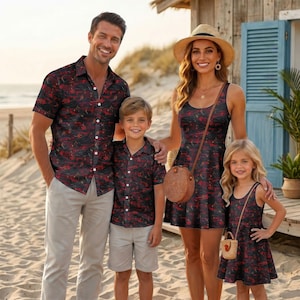 May include: A family wearing matching black shirts and dresses with a red and dark pattern. The adult wears a short-sleeve button-down shirt and light pants, while the child wears a matching shirt and shorts. The adult and child wear matching dresses.