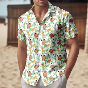 Puede incluir: Camisa blanca con botones con un patrón repetido de personajes de El Rey León. El diseño incluye a Simba, Pumbaa, Timón y hojas verdes. La camisa tiene mangas cortas y un cuello clásico.