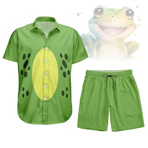 May include: A green frog-themed outfit, comprising a short-sleeved button-down shirt and matching shorts. The shirt has a yellow oval design with black spots, and the shorts have a drawstring. A watercolour illustration of a smiling frog is in the background.