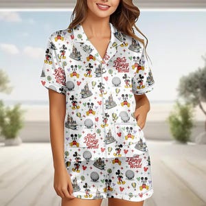 May include: White pajama set with a pattern of Mickey Mouse, castles, balloons, and the text "Walt Disney World." The short-sleeved top and shorts have white piping and a button-down front. The set is made of a soft, silky material.