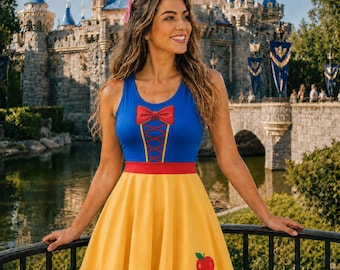 May include: A sleeveless dress featuring a blue bodice with a red bow and lace-up detail, a red waistband, and a yellow skirt with a red apple graphic. The dress has a scoop neckline and a flared silhouette, designed with a vibrant color palette.