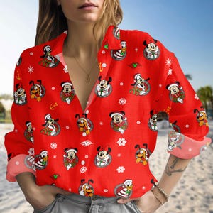 May include: A long-sleeved button-down shirt in bright red featuring an all-over print of Disney characters including Mickey Mouse, Minnie Mouse, Pluto, and Donald Duck wearing Santa hats, interspersed with white snowflakes and small anchor icons.