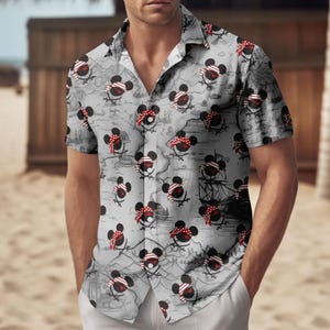 May include: Gray button-down shirt featuring a repeating pattern of cartoon pirate mice with red and white bandanas and eye patches. The background includes a map and pirate ship illustrations. The shirt has short sleeves.