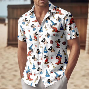 Op de afbeelding: Wit overhemd met korte mouwen met een herhaald patroon van Mickey Mouse in verschillende poses. Het ontwerp bevat Mickey in tovenaarsoutfits, met blauwe hoeden, rode gewaden en bezems. Het overhemd heeft een klassieke kraag.