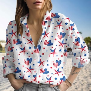Puede incluir: Camisa blanca abotonada con un estampado patriótico de estrellas y corazones rojos y azules. La camisa de manga larga tiene un cuello clásico y está desabrochada en el escote.