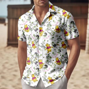 May include: White short-sleeved shirt with a repeating pattern of a yellow bear in a pink shirt, honey pots, flowers, and the text "save the bees". The shirt has a classic collar.