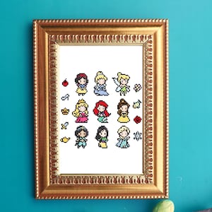 Puede incluir: Una obra de arte en punto de cruz enmarcada con imágenes pixeladas de varias princesas. La obra de arte se muestra en un marco dorado adornado. Las princesas están representadas con sus trajes y peinados característicos, con pequeños iconos.