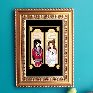 以下が含まれることがあります： 伝統的な衣装を着た2人の人物を描いた、額入りのピクセルアートプリント。一人は赤、もう一人は白を着用しています。アートワークは黒い背景にあり、金色の装飾フレームに入っています。プリントはターコイズの壁に表示されています。