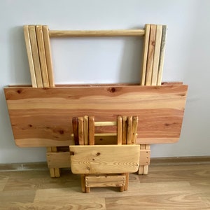 Könnte beinhalten: Ein Klapptisch- und Stuhlset aus Holz. Der Tisch ist aus hellem Holz und hat ein schlichtes Design. Der Stuhl ist ebenfalls aus hellem Holz und hat ein schlichtes Design. Tisch und Stuhl sind zusammengeklappt und übereinander gestapelt.