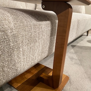 Puede incluir: Una mesa auxiliar de madera con base cuadrada y pata curva. La encimera rectangular es de madera m&aacute;s clara. La mesa est&aacute; dise&ntilde;ada para deslizarse debajo de un sof&aacute;. Medidas en cent&iacute;metros.