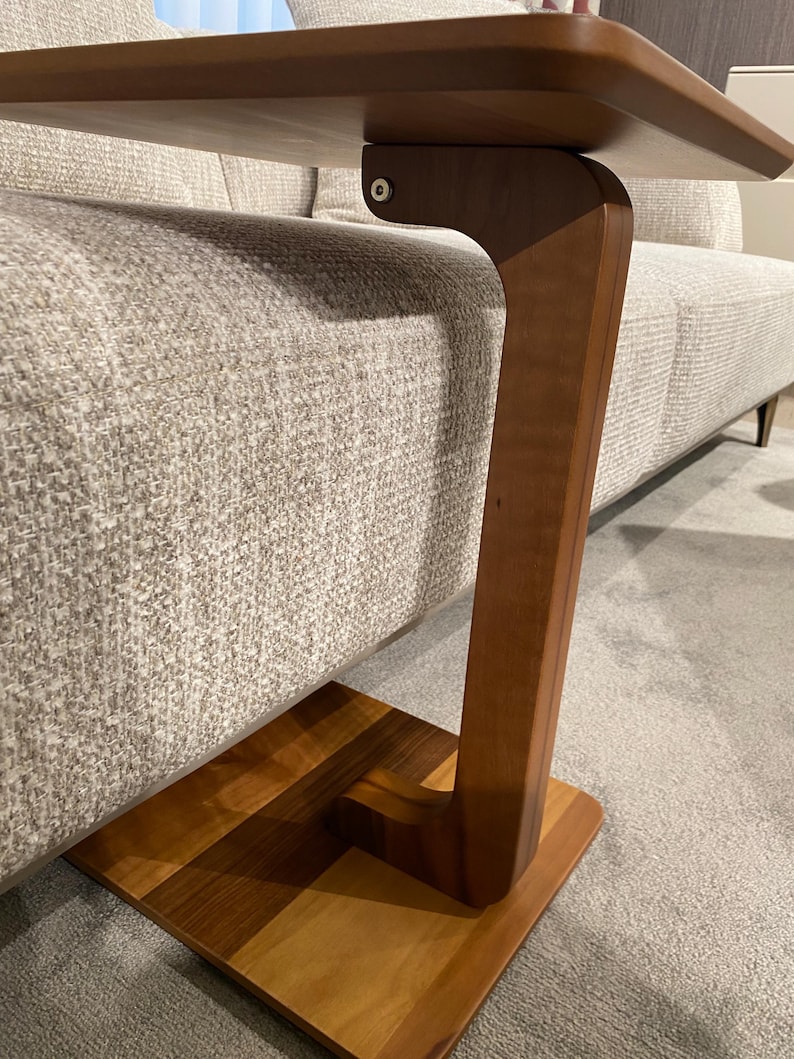 Puede incluir: Una mesa auxiliar de madera con base cuadrada y pata curva. La encimera rectangular es de madera m&aacute;s clara. La mesa est&aacute; dise&ntilde;ada para deslizarse debajo de un sof&aacute;. Medidas en cent&iacute;metros.
