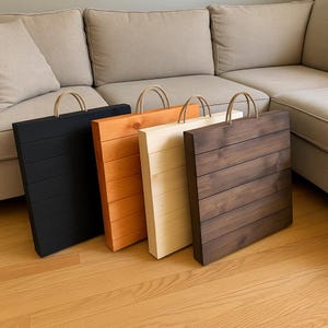 May include: Four wooden serving trays with rope handles in black, orange, natural, and dark brown. Each tray has a rectangular shape with horizontal wooden slats. The trays are displayed on a wooden floor.