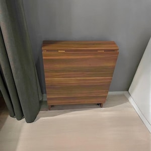 May include: A brown wooden folding table with a wood grain pattern. The table is closed and has a simple design.