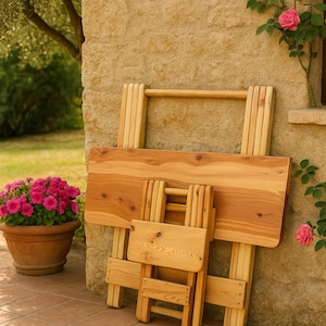 Könnte beinhalten: Ein Set aus klappbaren Holzmöbeln, darunter ein Tisch und ein kleiner Stuhl, lehnt an einer Steinmauer. Das Naturholz hat eine hellbraune Farbe. Im Hintergrund ein Terrakottatopf mit rosa Blüten.