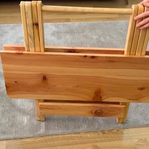 May include: A wooden folding table with a natural finish. The table has a single shelf and a handle for carrying.