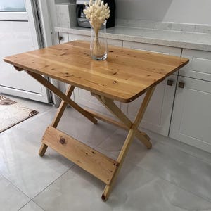 May include: A light wood folding table with a simple design. The table is made of natural wood and has a smooth finish. It is a great option for small spaces or for use as a temporary table.