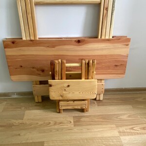 Pode incluir: Um conjunto de mesa e cadeira dobráveis de madeira. A mesa e a cadeira são feitas de madeira natural e estão em posição dobrada. A mesa e a cadeira são ambas de cor castanho claro.