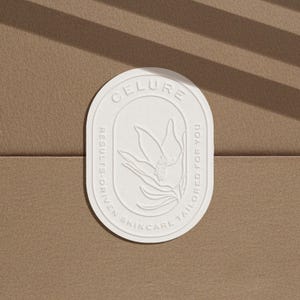Puede incluir: Pegatina ovalada blanca con el texto "CELURE RESULTS-DRIVEN SKINCARE TAILORED FOR YOU" y un diseño de flor estilizado.