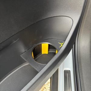 May include: A black car door interior with a yellow cup holder. The cup holder is located in the door panel and has a black rubber lining.