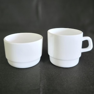 May include: Two white ceramic cups, one with a handle and the other without. The cup with the handle is stacked with two layers.