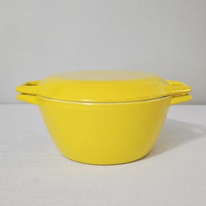 May include: A bright yellow, lidded casserole dish. The dish has a rounded bowl shape with two side handles. The lid is flat and fits snugly on top. The dish is made of a solid material and is suitable for cooking and serving.