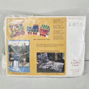 May include: A plastic-wrapped craft kit package labeled 1826 by The Creative Circle. The front displays images of a train, a waterfall, and a rug. Text includes design names like Choo Choo Train, Navajo Sands Pillow, and Navajo Sands Rug.