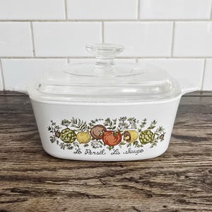May include: White casserole dish with a clear glass lid. The dish features a colorful vegetable design with the text "La Persil, La Sauge". The dish has handles on each side.
