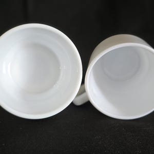May include: Two white ceramic mugs with a smooth, glossy finish. The mugs are empty and ready to be filled with a hot beverage.