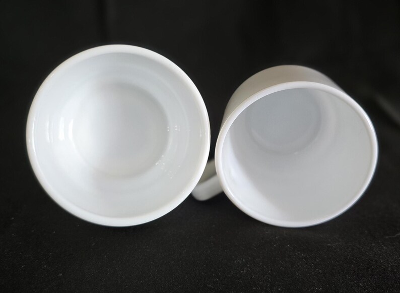 May include: Two white ceramic mugs with a smooth, glossy finish. The mugs are empty and ready to be filled with a hot beverage.