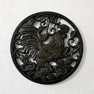May include: A circular dark brown metal wall plaque featuring an openwork design of a rooster standing among sunflowers and swirling vine patterns. The piece has a textured finish and is framed by a solid circular border, creating a detailed silhouette.