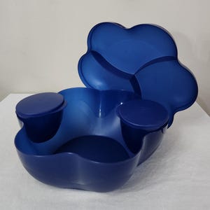 May include: A blue plastic serving bowl with three smaller bowls attached. The bowl has a matching lid with four sections.