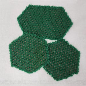 May include: Three green crocheted doilies with a red flower pattern. The doilies are hexagonal in shape and have a fringed edge.