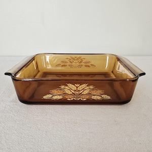 May include: A rectangular amber-colored glass baking dish with a wheat pattern. The dish has a brown exterior and a lighter amber interior. The wheat design is in shades of gold and brown, adding a vintage touch to the bakeware.