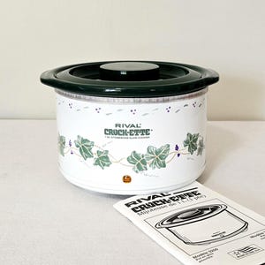 May include: A white Rival Crock-Ette 1 litre stoneware slow cooker with a dark green lid and a green ivy vine pattern. The front features the text Rival Crock-Ette 1 Qt. Stoneware Slow Cooker and a small orange indicator light, with an instruction manual.