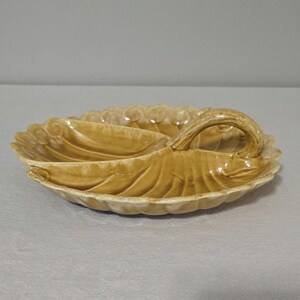May include: A tan ceramic leaf-shaped serving dish with three compartments and a handle. The dish has a scalloped edge and detailed leaf vein patterns. The handle is curved and integrated into the leaf design. This decorative dish is suitable for serving snacks or appetizers.