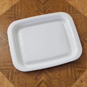 May include: A white ceramic butter dish with a raised rim and a smooth, glossy finish.