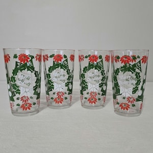 May include: Four clear drinking glasses with a Christmas theme. Each glass features a design of red poinsettias, green holly leaves, and the words "Merry Christmas" in a white banner. The glasses are cylindrical and appear to be made of glass.
