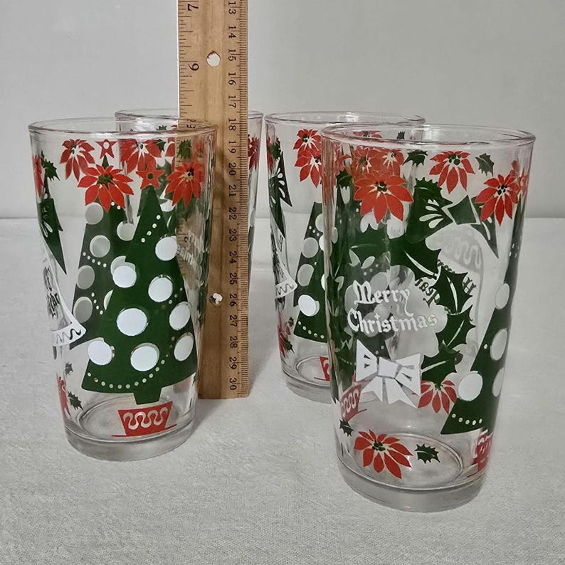 May include: Set of four clear drinking glasses with Christmas tree and poinsettia designs. Each glass features a green Christmas tree with white polka dots, red poinsettias, and the text "Merry Christmas".